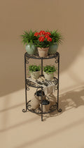 Three-tier iron scrollwork plant stand with potted plants and garden baskets on warm beige background