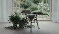 Cast iron leaf accent table with scrollwork legs styled with ferns and ivy by a garden window